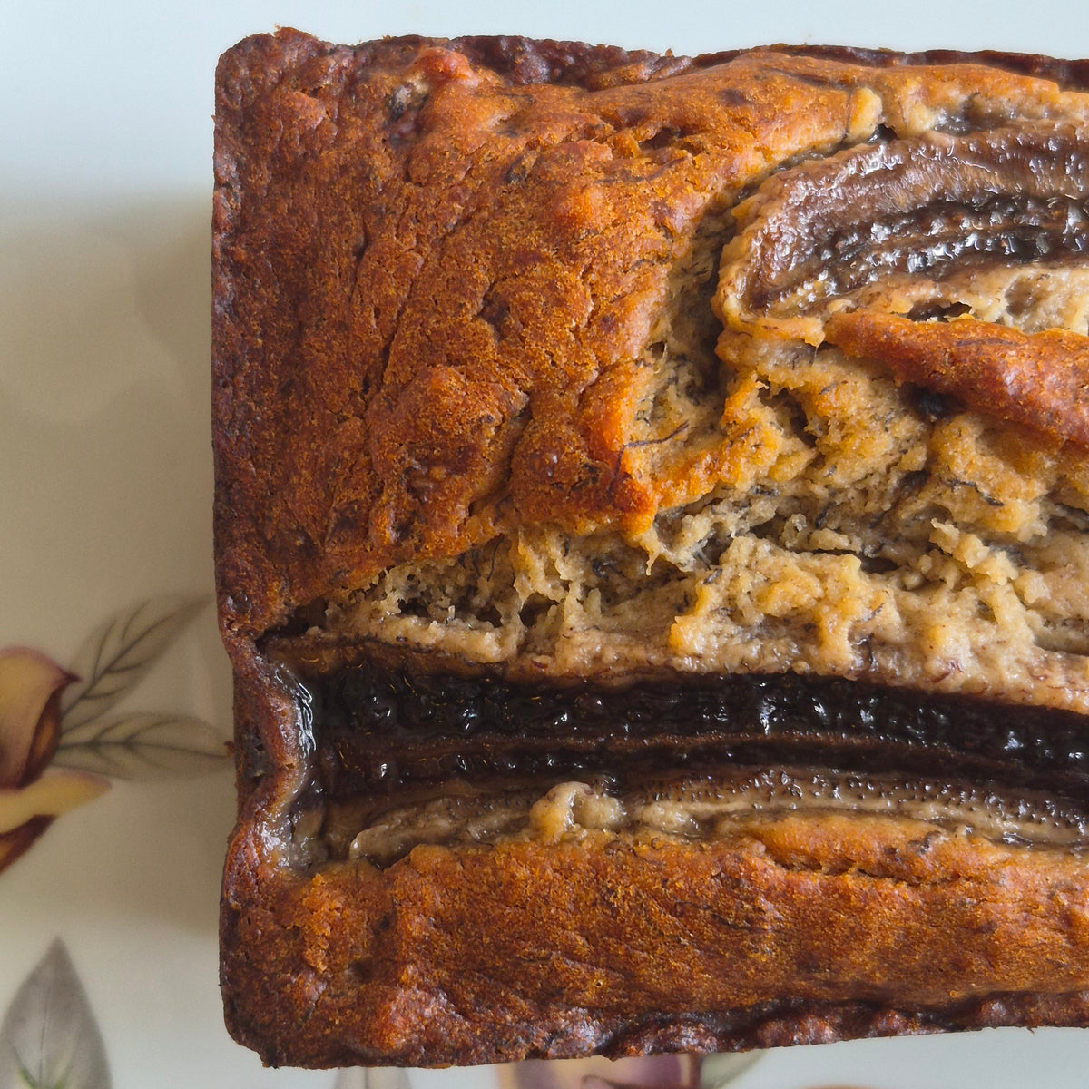 A close-up top-down view of a freshly baked loaf of banana bread on a floral-patterned plate.