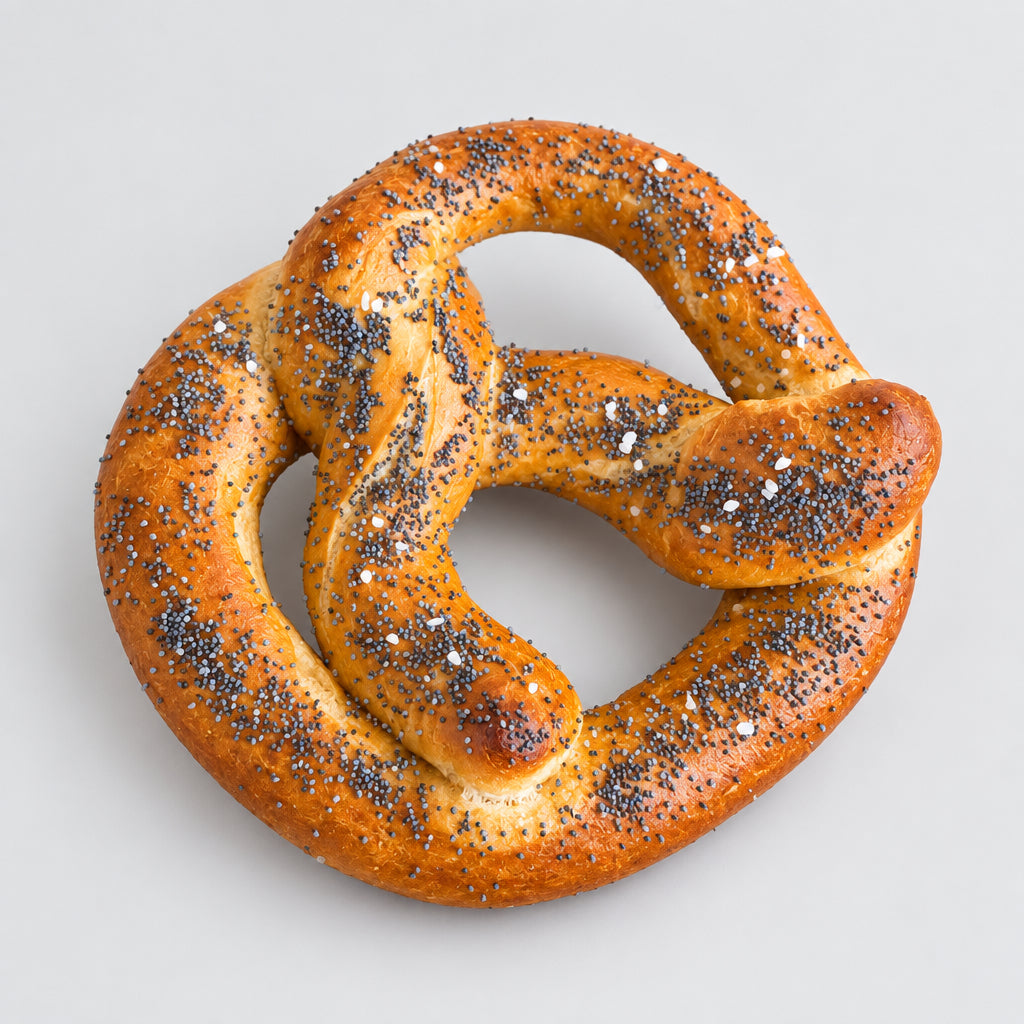 A large baked pretzel with poppy seeds and coarse salt, presented on a rustic wooden serving board over a light stone surface.